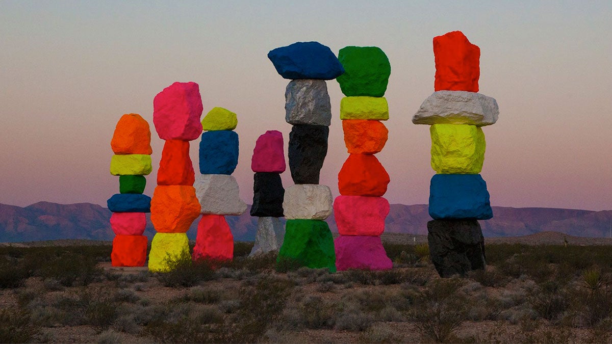 muticolored art installation in desert lands with pink sky and mountains in background at Seven Magic Mountains Installation, Las Vegas, Nevada, USA