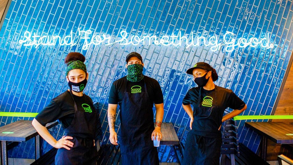 Shake Shack employees under neon Stand For Something Good sign on blue tile wall