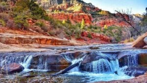 rock formations with trees and greenery and rushing water in the foreground - Sedona, Arizona, USA