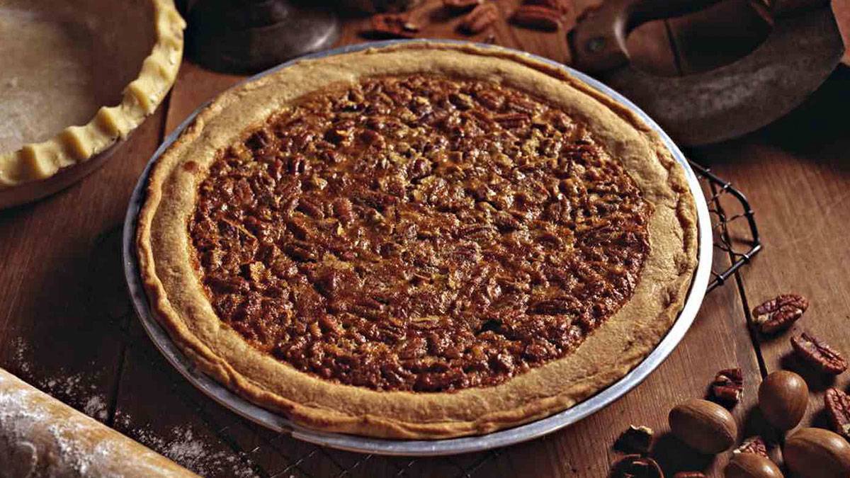close up of pecan pie on cooling rack beside pie crust, rolling pin, and pecan nuts on wooden table for Thanksgiving at Colonial Williamsburg's Pie Sale in Williamsburg, Virginia, USA