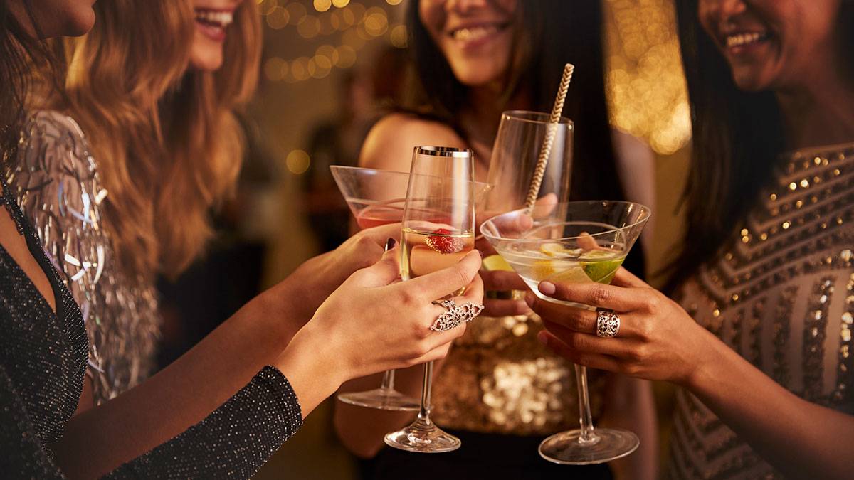 smiling women in party dresses, toasting with drinks