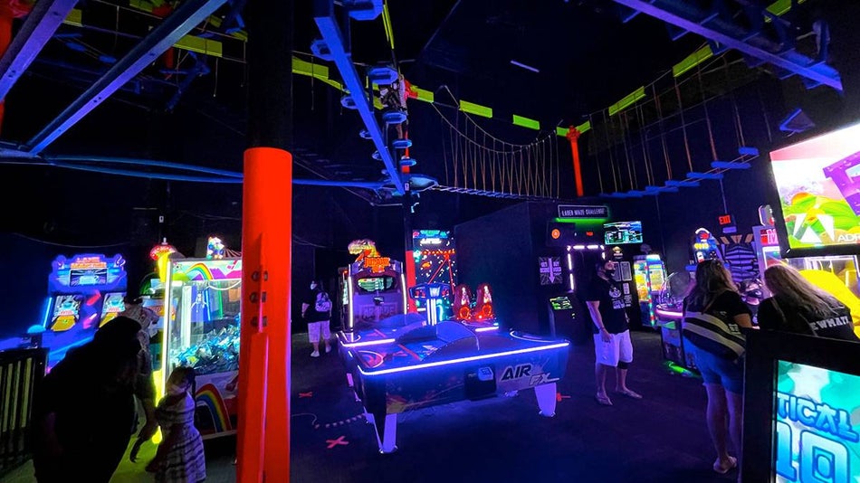 people in blacklight room filled with arcade games and attractions with neon decorations at WonderWorks Arcade in Orlando, Florida, USA