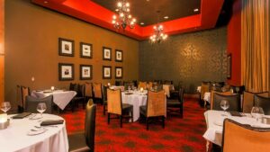 Wide shot a dining room with red and black carpet with black walls and a black ceiling with red accents, there are also several white cloth covered tables with black and brown chairs at Level 2 Steakhouse in Branson, Missouri, USA