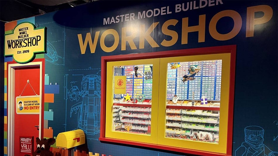 Entrance to the Master Model Builder Workshop, a blue Wass with lego schematics on it and yellow pained windows where you can see a wall of legos thought the window at the LEGOLAND Discovery Center in Chicago, Illinois, USA