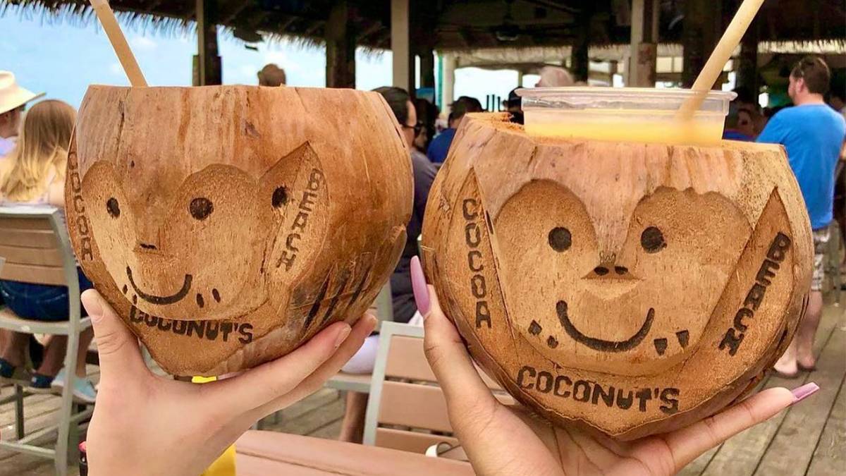 Close up of two coconuts with drinks in them and they have smiley faces carved into them with people in the background at Coconuts on the Beach Restaurant in Cocoa Beach, Florida, USA