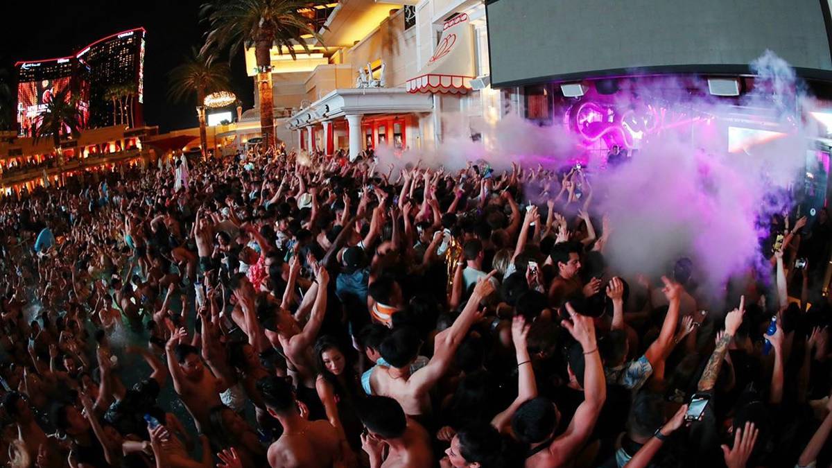 A large crowd of people, some of them shirtless, partying at Encore Beach Club with purple smoke over the crowd at night in Las Vegas, Nevada, USA
