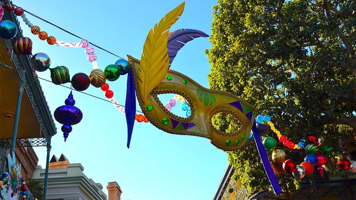 View looking up at a giant Mardi Gras mask hanging over New Orleans Square with lots of other bright decorations on a sunny day at Disneyland in Los Angeles, California, USA