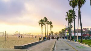 Wide shot of the Venice Beach Boardwalk with people playing volleyball and skating at sunset near Los Angeles, California, USA