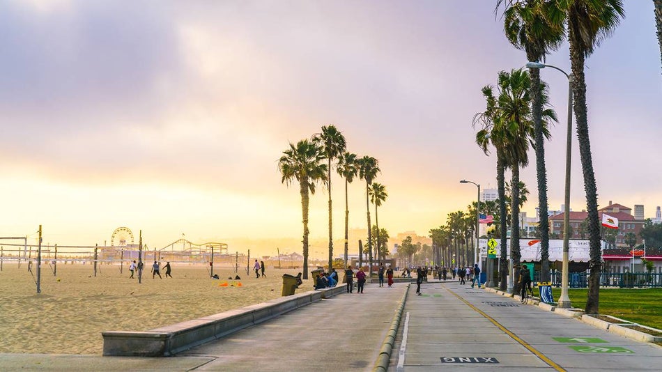 Wide shot of the Venice Beach Boardwalk with people playing volleyball and skating at sunset near Los Angeles, California, USA