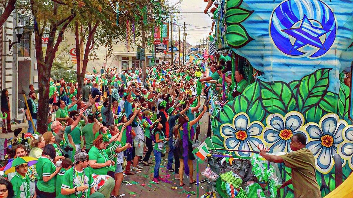 Wide shot of a street full of people wearing green and a giant parade float throwing beads that the St Patrick's Day Parade in New Orleans, Louisiana, USA