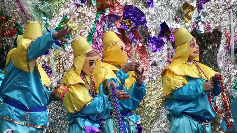 Close up of four people in full green, yellow, and purple Mardi Gras costumes handing out beads in New Orleans, Louisiana, USA