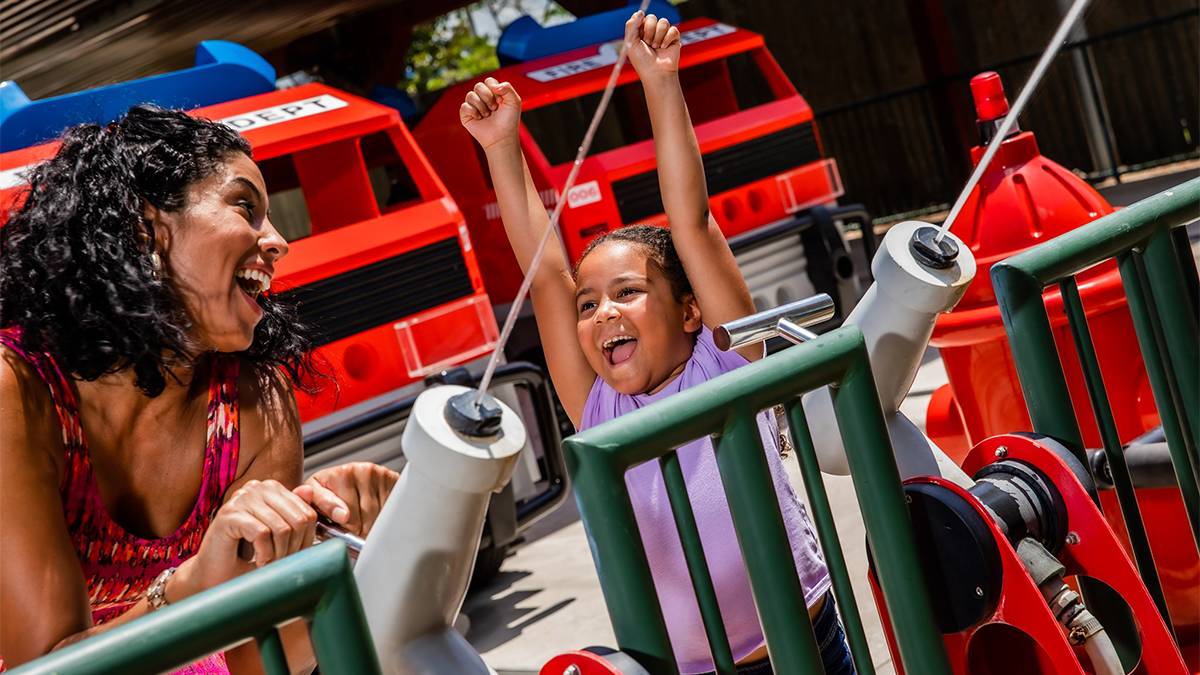 A mom and her daughter shooting water guns with fire trucks behind them on Hero's Weekend at LEGOLAND Florida in Orlando, Florida, USA