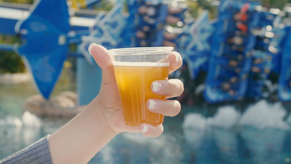Close up of a women's hand holding a cup of beer in front of a roller coaster at the Craft Beer Festival at SeaWorld in Orlando, Florida, USA
