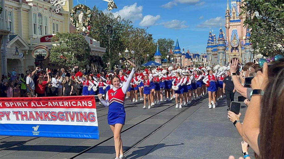 Cheerleaders marching in the Disney Thanksgiving Parade with a view of Cinderella's Castle in the background on a sunny day in Orlando, Florida, USA