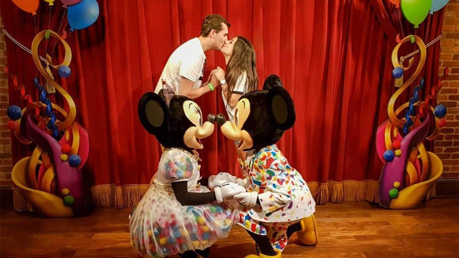A couple kissing in front of a red curtain and Mickey and Minnie kneeling and touching their noses together at Walt Disney World in Orlando, Florida, USA