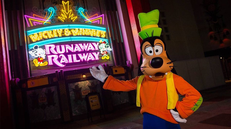Close up of Goofy pointing to the neon sign for Mickey and Minnie's Runaway Railway at night in Orlando, Florida, USA