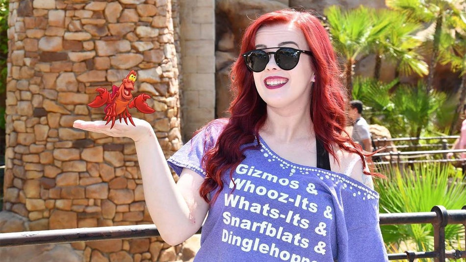Close up of a woman with bright red hair and a purple Ariel shirt with her hand out with a PhotoPass filter on it to make it look like she is holding Sebastian at Walt Disney World in Orlando, Florida, USA