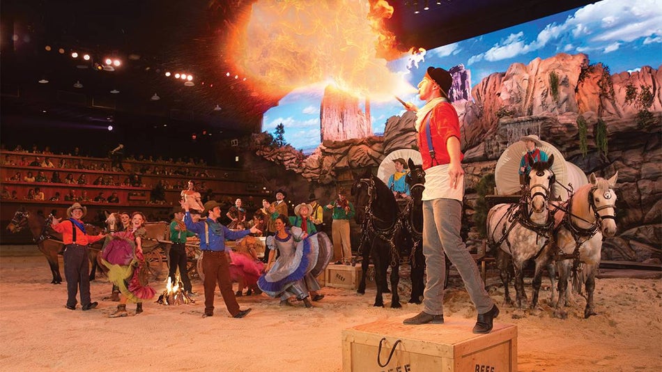 Close up of a man breathing fire with wagons and people dressed in old western clothes behind him at the Dolly Parton Stampede in Pigeon Forge, Tennessee, USA