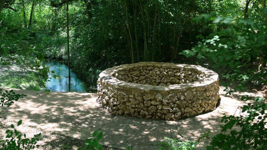 Close up of a stone well surrounded by trees with water in the background at Headwaters Sanctuary in San Antonio, Texas, USA