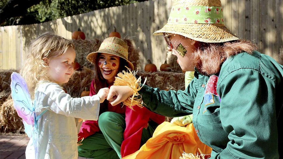 Close up of a toddler in a butterfly costume fist bumping an adult dressed as a scarecrow with another scarecrow in the back ground during Spooktacular at SeaWorld in San Antonio, Texas, USA