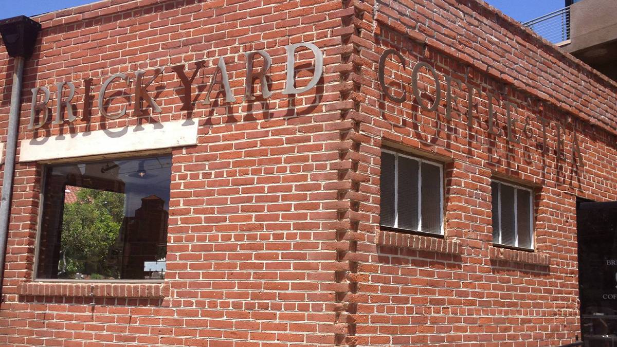Close up of the red brick building for Brickyard Coffee and Tea with their metal sign rounding the corner in San Diego, California, USA