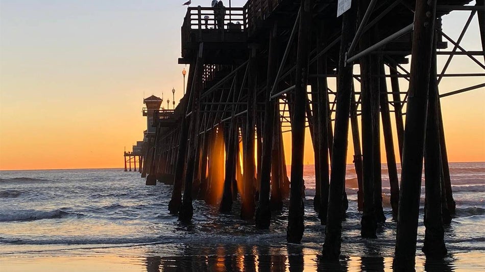View of the water and a light orange sunset from the under the Oceanside Municipal Pier in San Diego, California, USA