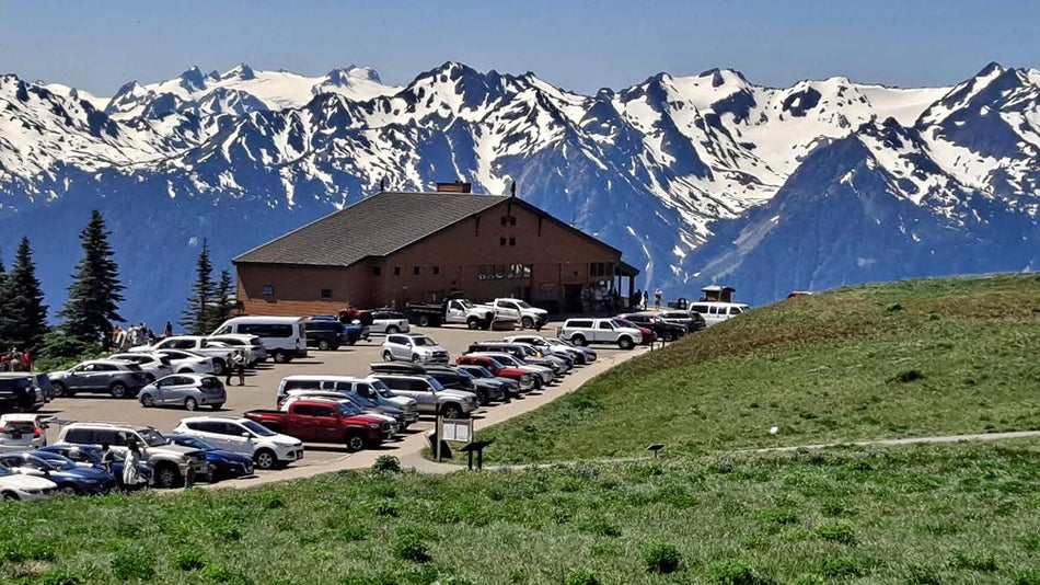 Wide shot of the Olympic Park Visitor Center with a parking lot full of cars and snowy mountains behind it near Seattle, Washington, USA