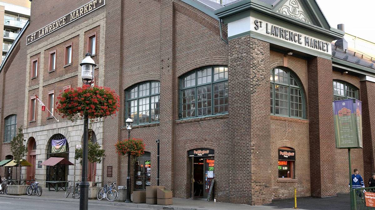 Close up of the corner of the St Lawrence Market building, a large brick building with a green roof and light poles on the outside with flowers on then in Toronto, Ontario, Canada