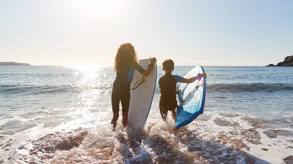 Close up of two children with surfboards walking into the ocean on a sunny day.