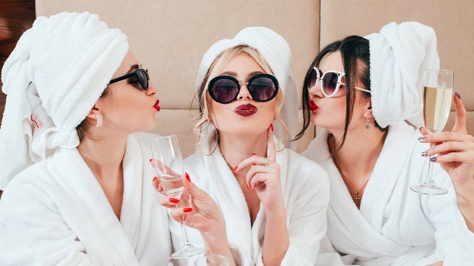 Close up of three women with sunglasses and red lips in hair towels and white robes at the spa